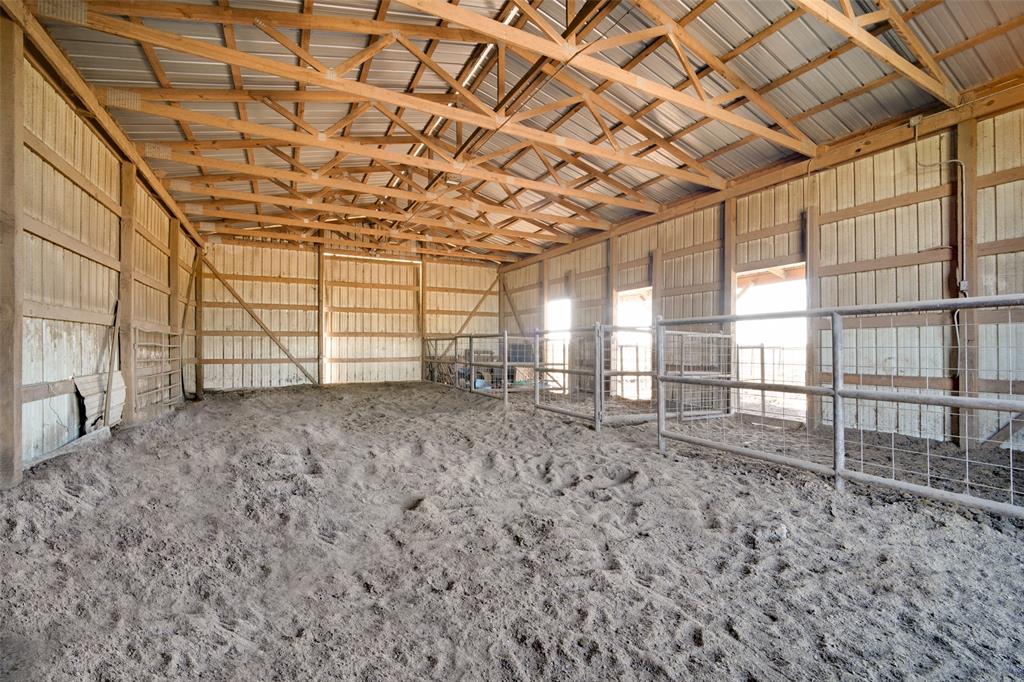 Open-span barn featuring exposed wood-truss ceiling, metal roofing, and built-in metal stall partitioning, and  built in cattle cradle on the outside.