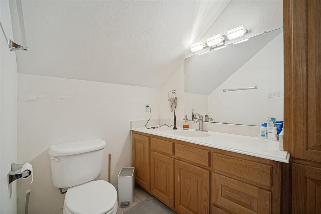 Bathroom featuring a wood-finish vanity with a solid-surface integrated sink, large wall-mounted mirror, three-light fixture, and architectural sloped ceiling