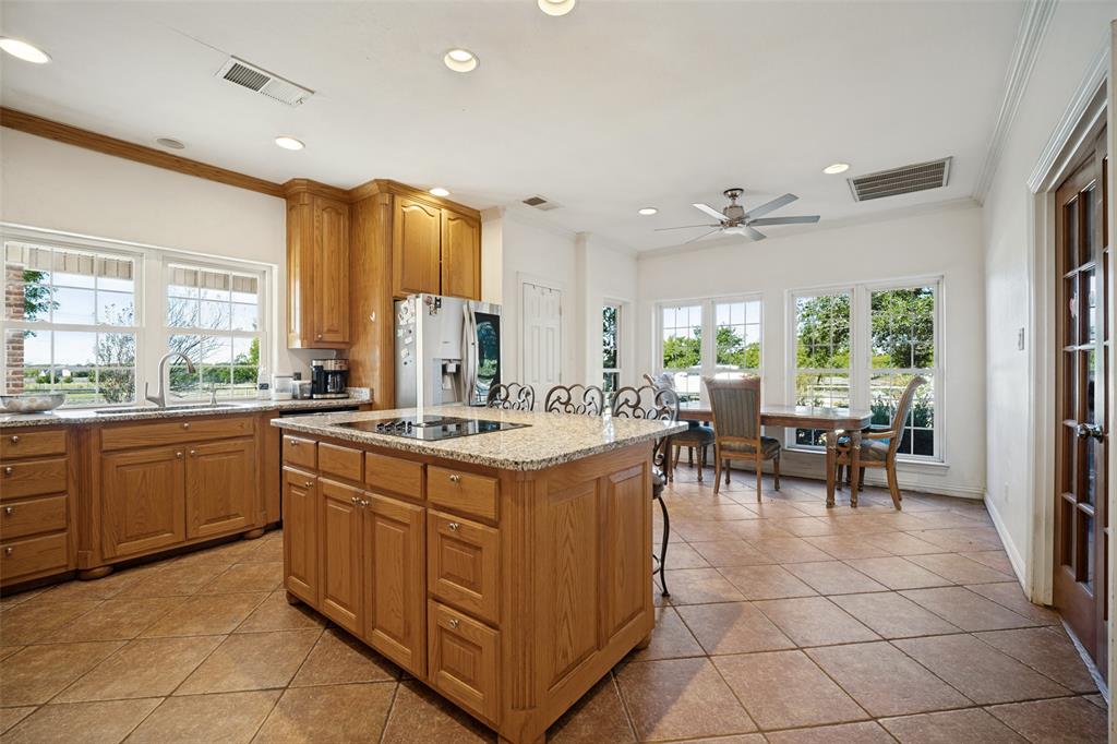 Kitchen featuring wood cabinetry, stone countertops, a center island with a built-in cooktop, tiled flooring, and recessed lighting