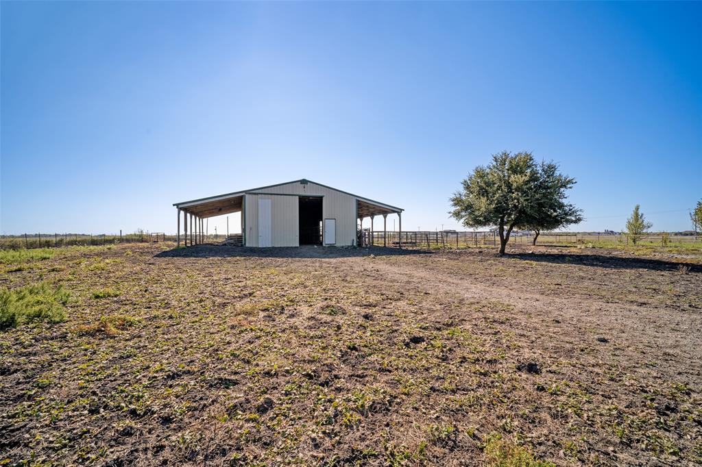 Metal-clad barn featuring covered side overhangs, a central drive-through bay, exterior holding areas and surrounding acreage.