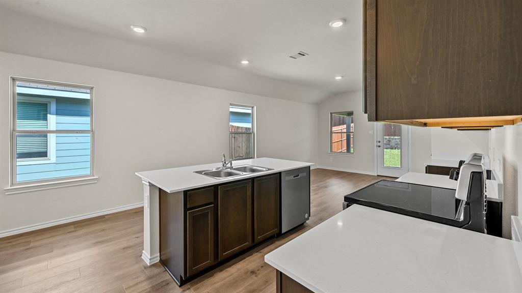 Kitchen island with double basin sink, white countertops, wood-finish flooring, and recessed lighting