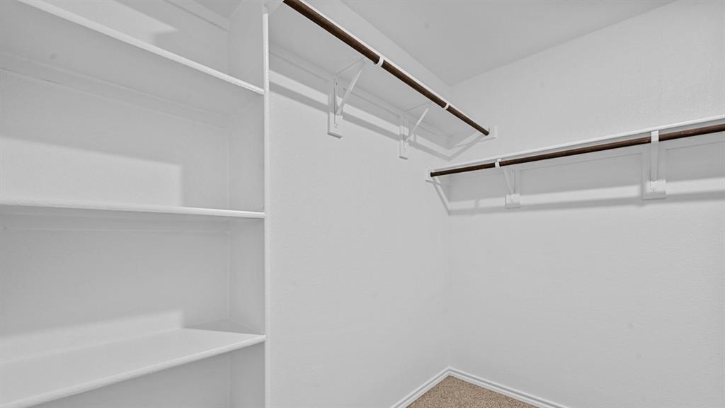Spacious walk-in closet featuring built-in shelving, dual hanging rods with metal brackets, and wood-finish flooring throughout