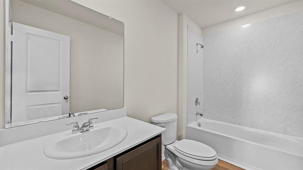 Bathroom featuring a single vanity with an integrated sink, a large wall-mounted mirror, and a bathtub with a shower kit