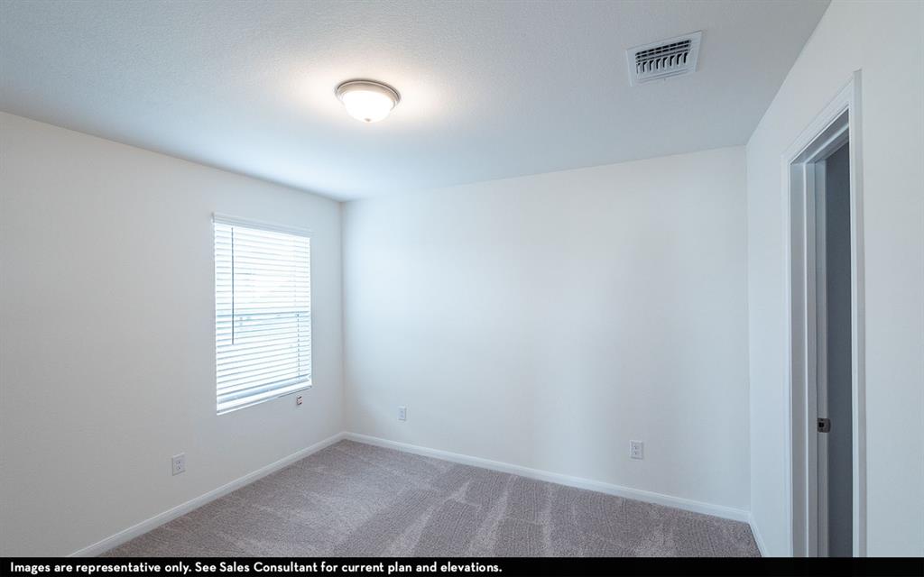 Neutral-toned interior space featuring wall-to-wall carpeting, a flush-mount overhead light fixture, and a window with horizontal blinds