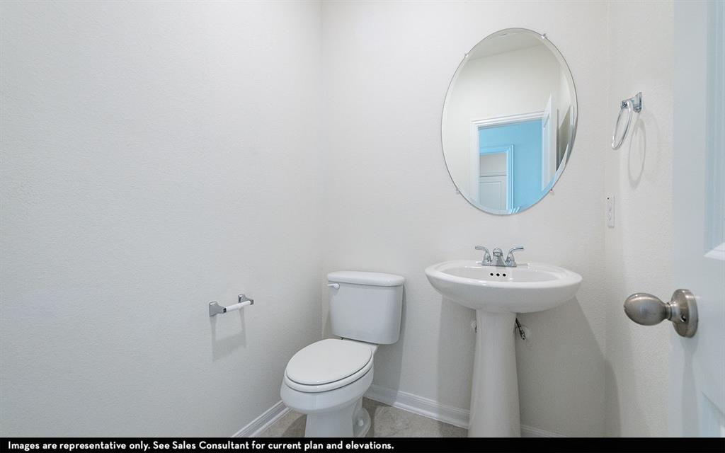 Powder room featuring a white pedestal sink, chrome hardware, oval wall-mounted mirror, and a standard-height toilet