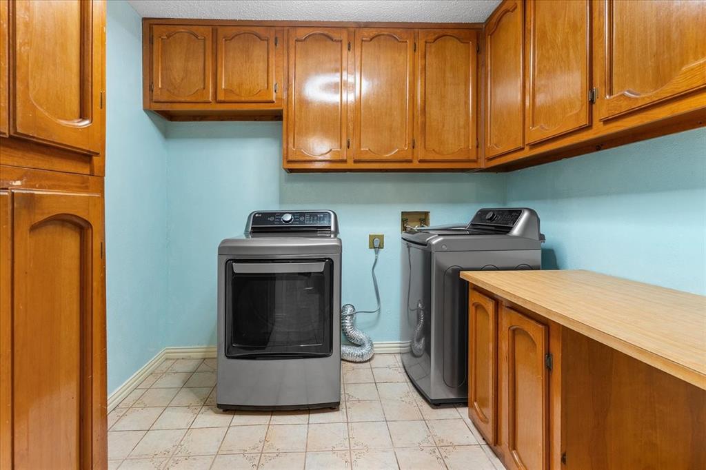 Utility room featuring wood-finish cabinetry, ample overhead storage, built-in counter space, and tiled flooring
