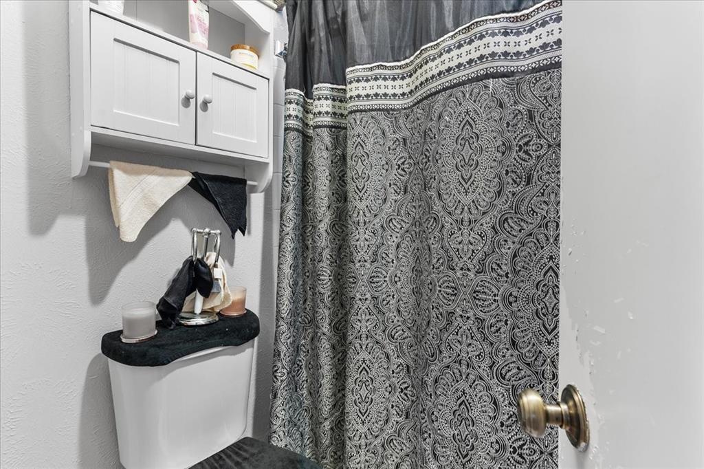 Wall-mounted wooden cabinet with dual doors and an open lower shelf, positioned above a standard toilet