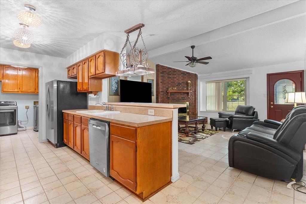 Kitchen featuring wooden cabinetry, a peninsula countertop, and integrated stainless steel dishwasher, with a brick fireplace and decorative pendant lighting