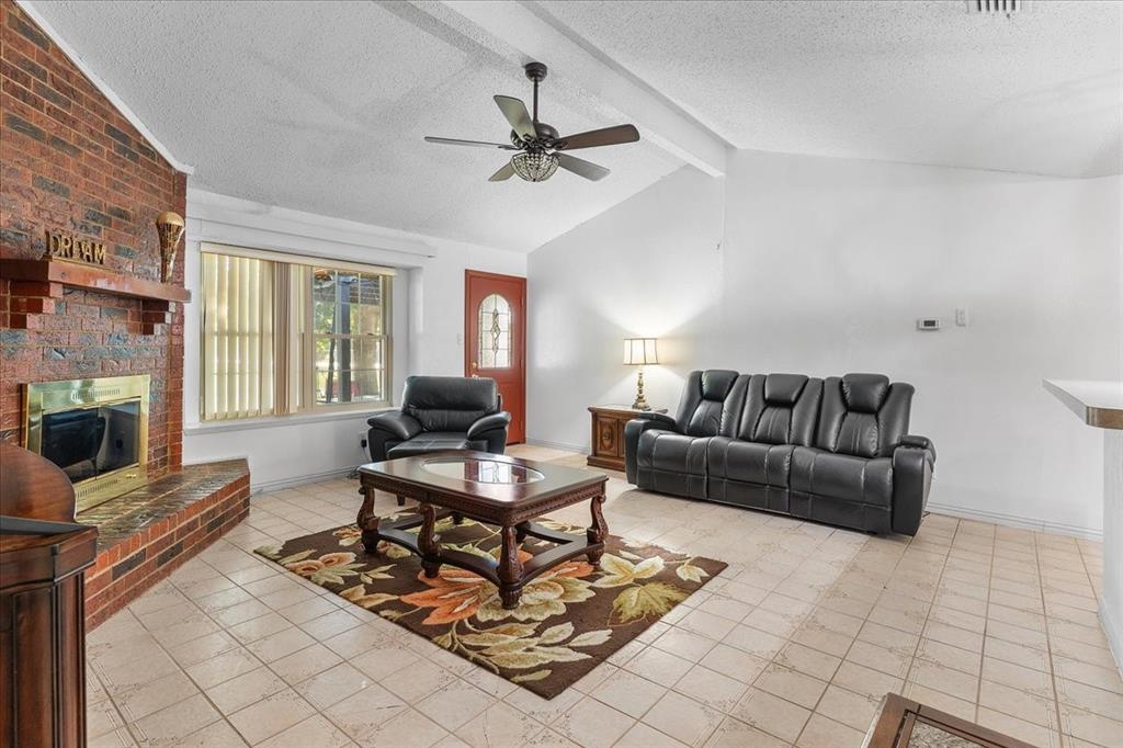 Vaulted ceilings with exposed beams, brick fireplace featuring a wood mantel and raised hearth, neutral tile flooring, and multi-paned glass entry door Vaulted ceilings with exposed beams, brick fireplace featuring a wood mantel and raised hearth, neutral tile flooring, and multi-paned glass entry door