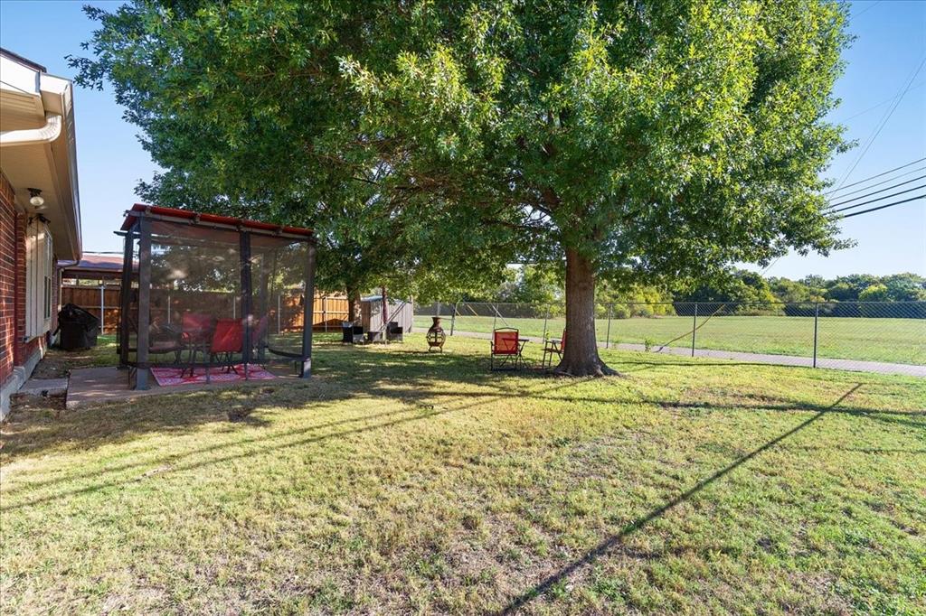 Spacious backyard featuring a large mature tree, a paved patio area, and perimeter chain-link fencing