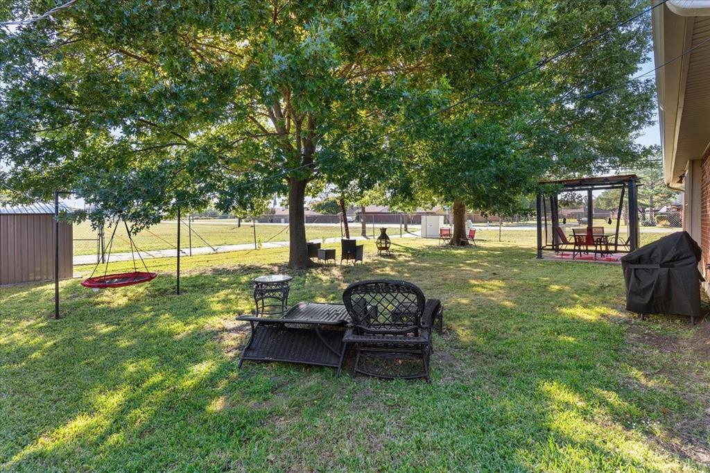 Expansive backyard featuring mature shade trees, a metal storage shed, and a metal-frame pergola