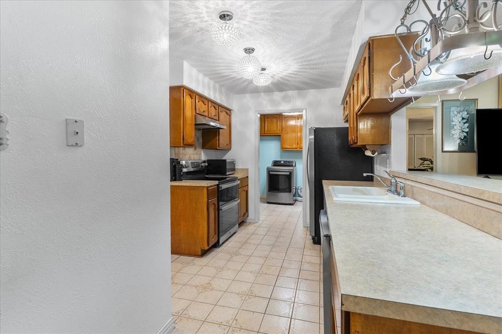 Kitchen featuring wood cabinetry, tile flooring, laminate countertops, a dual-basin sink, and multi-light ceiling fixtures