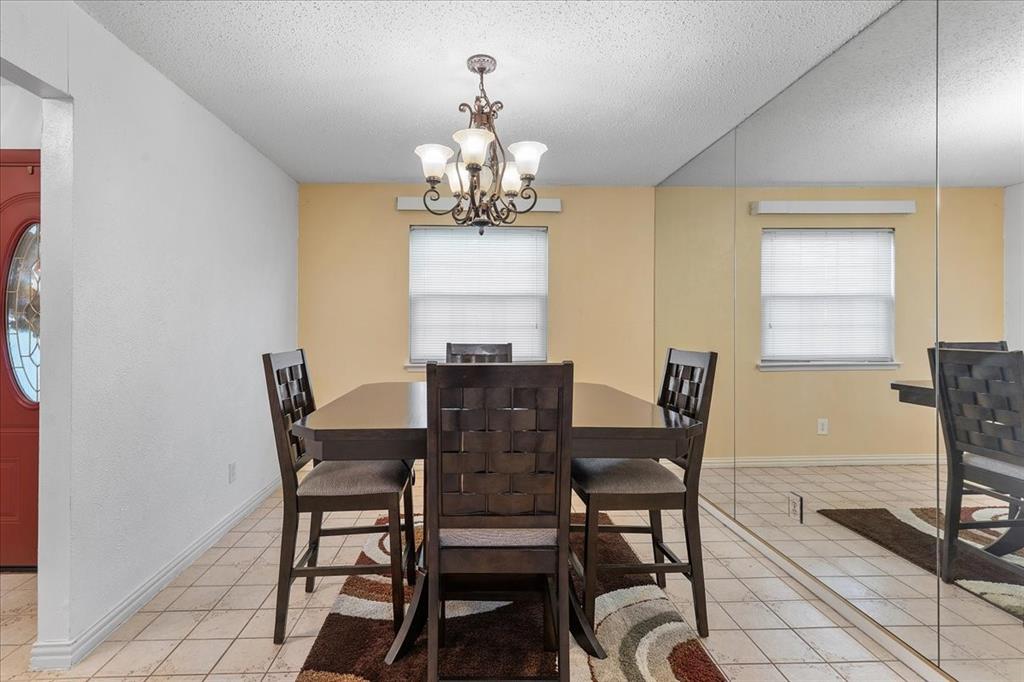 Dining area featuring large-scale wall mirrors, a multi-arm chandelier with glass shades, neutral ceramic tile flooring, and a window with blinds