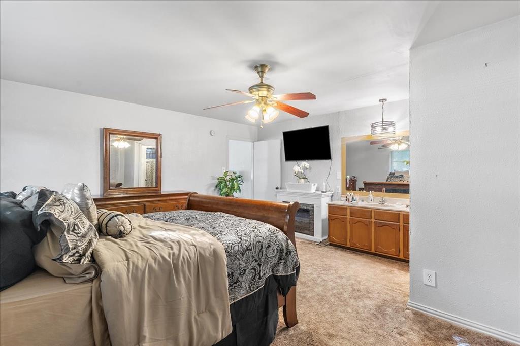 Bedroom featuring a multi-light ceiling fan, integrated electric fireplace, and built-in vanity cabinet with a large framed mirror and dual-light fixture
