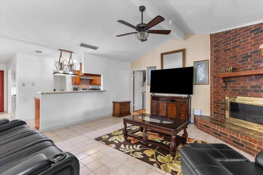 Living area featuring a floor-to-ceiling red brick fireplace with a wood mantel, vaulted ceilings with a center fan, tiled flooring, and a pass-through window with a breakfast bar