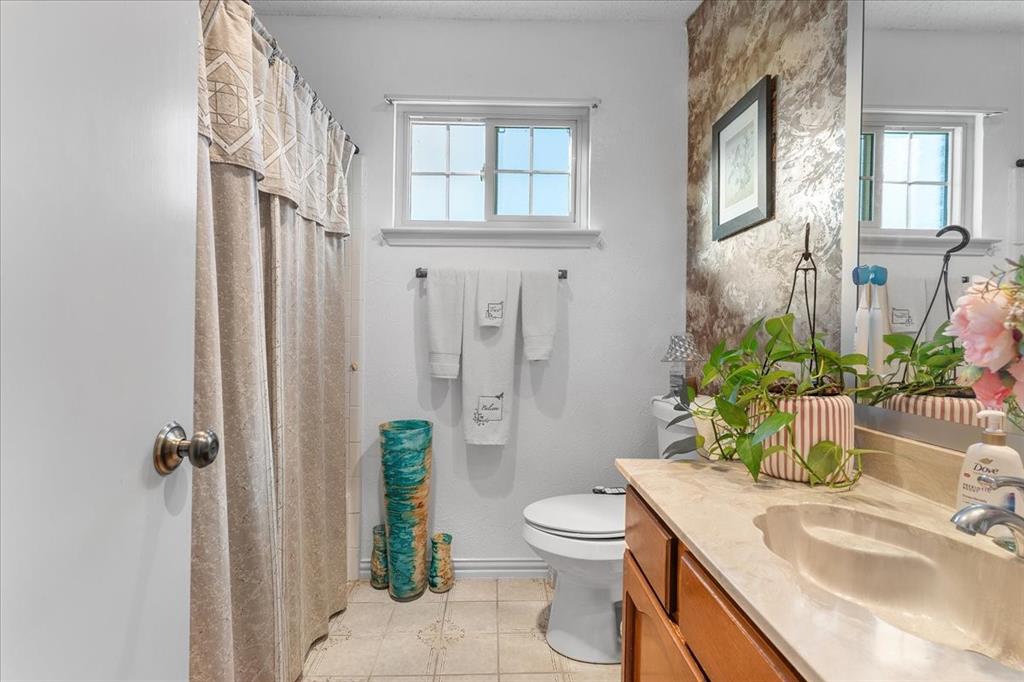 Bathroom featuring a vanity with a light-toned countertop, integrated basin, and wood-finish cabinetry, paired with a wall-mounted towel bar, a single-hung window, and a shower area Bathroom featuring a vanity with a light-toned countertop, integrated basin, and wood-finish cabinetry, paired with a wall-mounted towel bar, a single-hung window, and a shower area