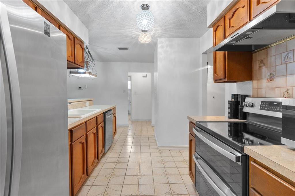 Kitchen featuring wooden cabinetry, stainless steel appliances, a tiled backsplash, and a spherical semi-flush mount light fixture