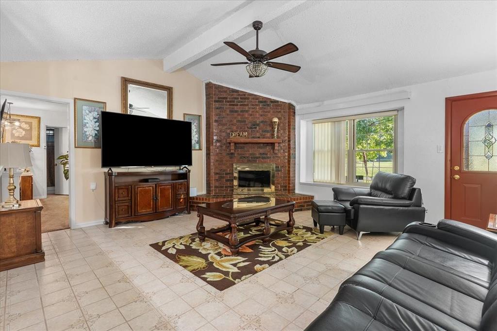 Living area featuring vaulted ceilings, floor-to-ceiling brick fireplace with wood mantel, tile flooring, and multi-pane entry door Living area featuring vaulted ceilings, floor-to-ceiling brick fireplace with wood mantel, tile flooring, and multi-pane entry door