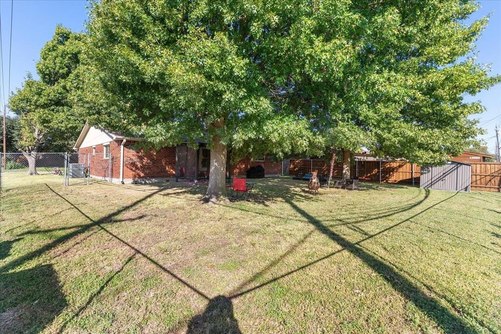 Fenced backyard featuring mature trees, brick exterior construction, and a metal storage shed