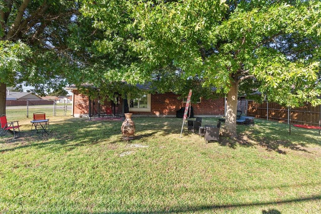 Rear exterior featuring red brick masonry, mature shade trees, a covered patio area, and perimeter wood fencing