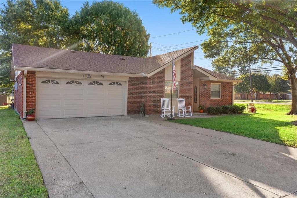 Single-story brick exterior featuring an attached two-car garage with arched panel detailing, a steep-pitched roofline, and a concrete driveway Single-story brick exterior featuring an attached two-car garage with arched panel detailing, a steep-pitched roofline, and a concrete driveway