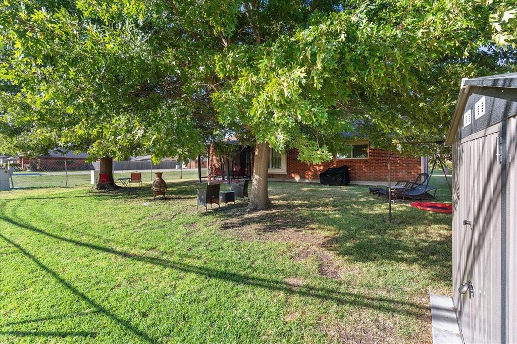 Expansive backyard featuring a lawn, mature trees, brick exterior cladding, and an outdoor storage structure