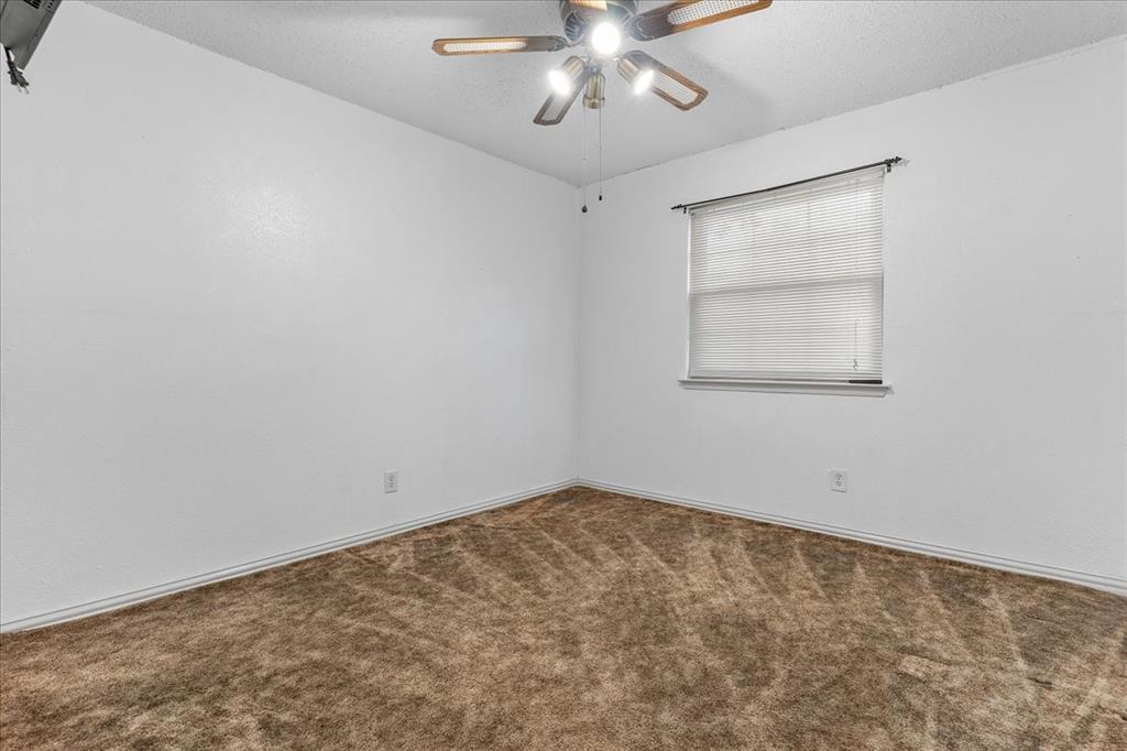 Neutral-toned carpeting, textured ceiling, ceiling fan with integrated lighting, and a single-pane window with horizontal blinds Neutral-toned carpeting, textured ceiling, ceiling fan with integrated lighting, and a single-pane window with horizontal blinds