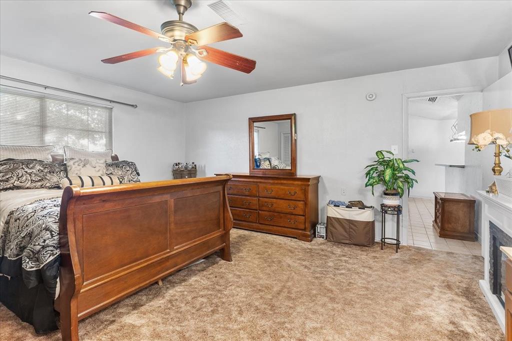 Spacious room featuring carpeting, a ceiling fan with integrated lighting, and a fireplace with a decorative mantel