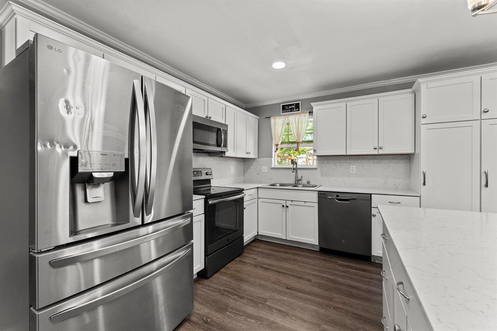Kitchen featuring white shaker-style cabinetry, stainless steel appliances, quartz countertops, and wood-finish flooring