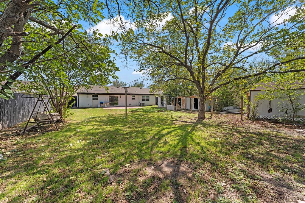 Backyard featuring expansive lawn space, mature shade trees, perimeter fencing, and a detached storage structure