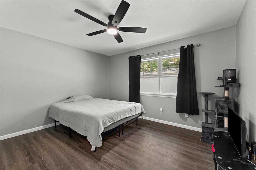 Bedroom featuring wood-finish flooring, a multi-blade ceiling fan with integrated lighting, and a dual-pane window