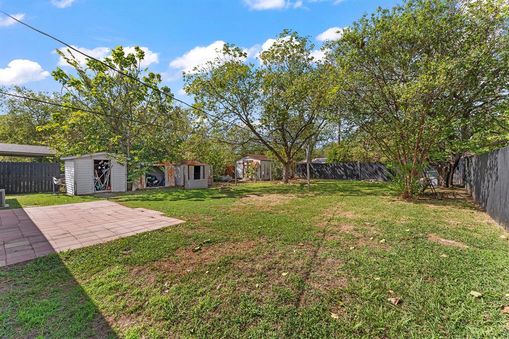 Expansive backyard featuring a paved patio, perimeter privacy fencing, and mature trees