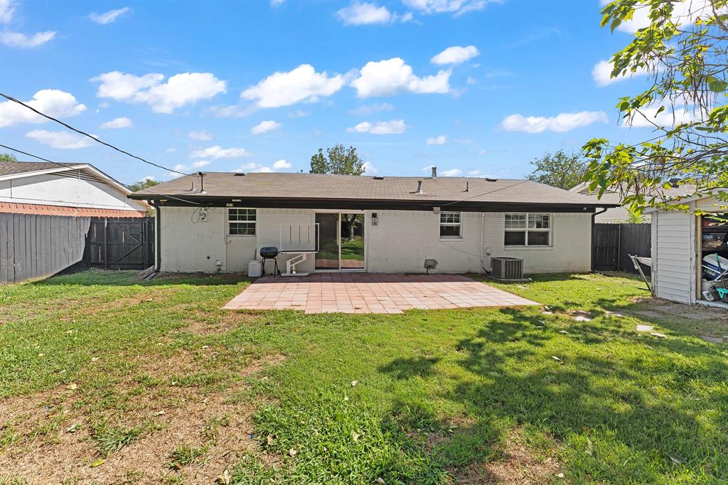 Rear exterior featuring a brick-paved patio, sliding glass door, and fenced perimeter