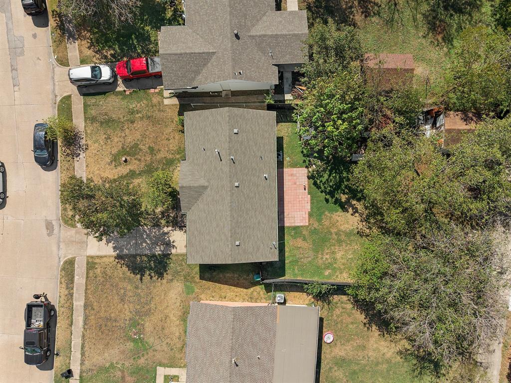 Aerial perspective featuring a residential lot with a brick-paved patio, mature trees, and perimeter fencing