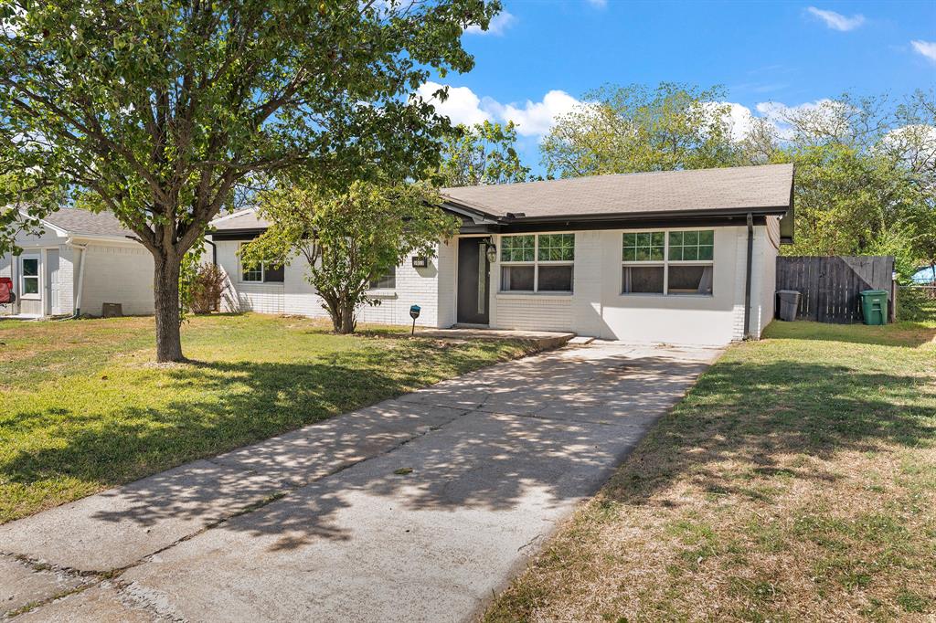 Single-story exterior featuring painted brick masonry, a concrete driveway, multi-pane windows, and a mature tree-lined landscape Single-story exterior featuring painted brick masonry, a concrete driveway, multi-pane windows, and a mature tree-lined landscape