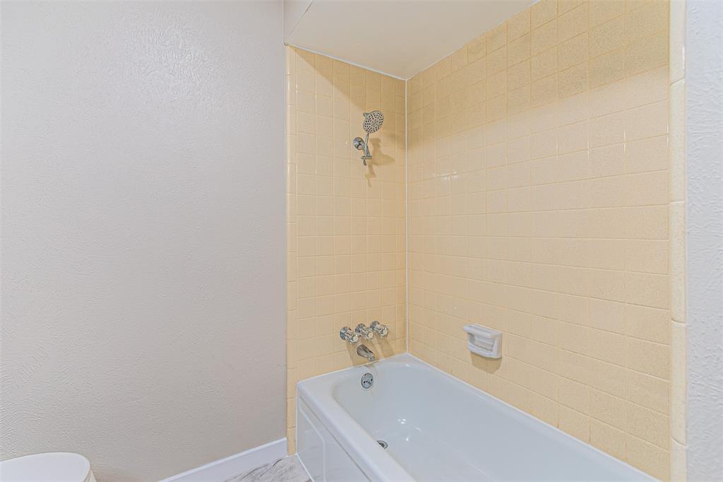 Bathtub with integrated shower, wall-mounted metallic fixtures, and tiled wall surround