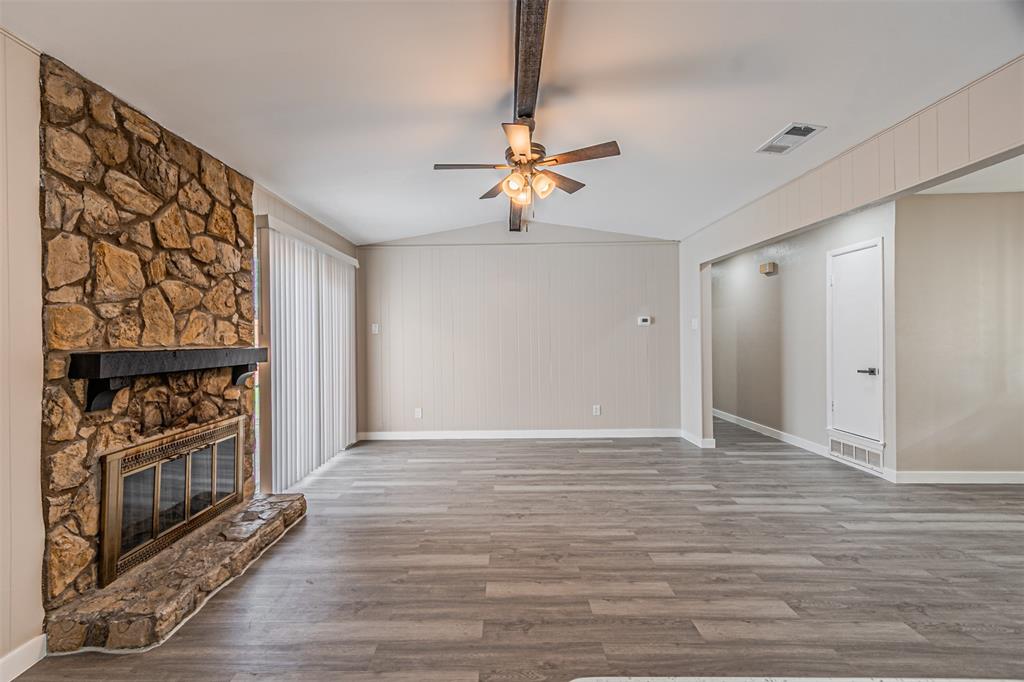 Living area featuring wood-finish flooring, a vaulted ceiling, floor-to-ceiling stone fireplace with a prominent mantel, and sliding glass doors