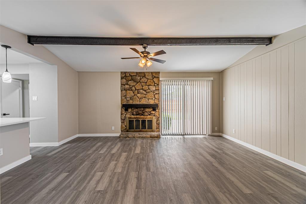 Living area featuring a natural stone fireplace, exposed structural steel beam, wood-finish flooring, and sliding glass doors