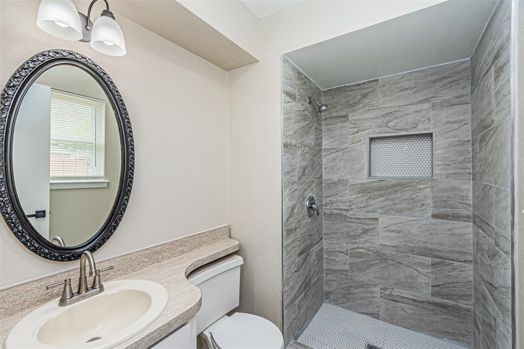 Bathroom featuring a walk-in shower with stone-patterned wall tile, a recessed niche, a neutral-toned countertop with an integrated basin, and an oval mirror with a decorative frame