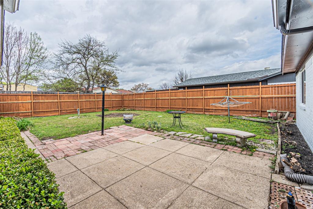 Backyard featuring a concrete patio, brick hardscaping, a wood privacy fence, and mature landscaping