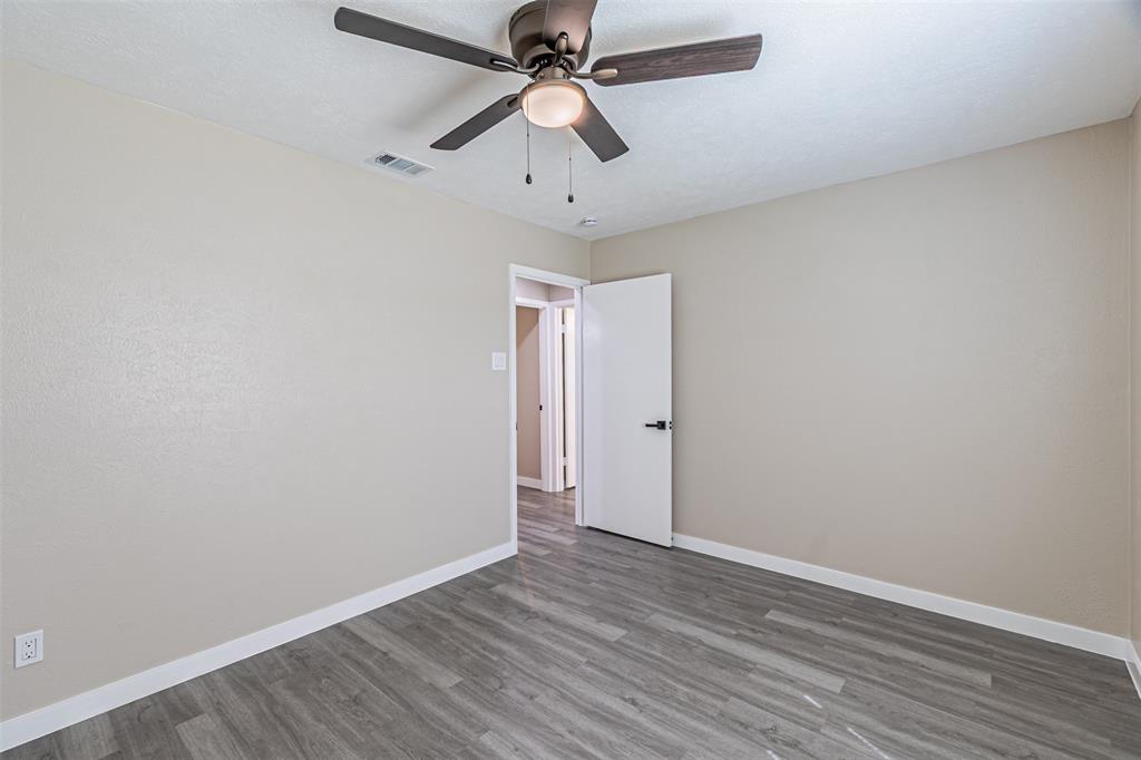 Room featuring wood-finish flooring, a ceiling fan with integrated lighting, and a white interior door with matte black hardware