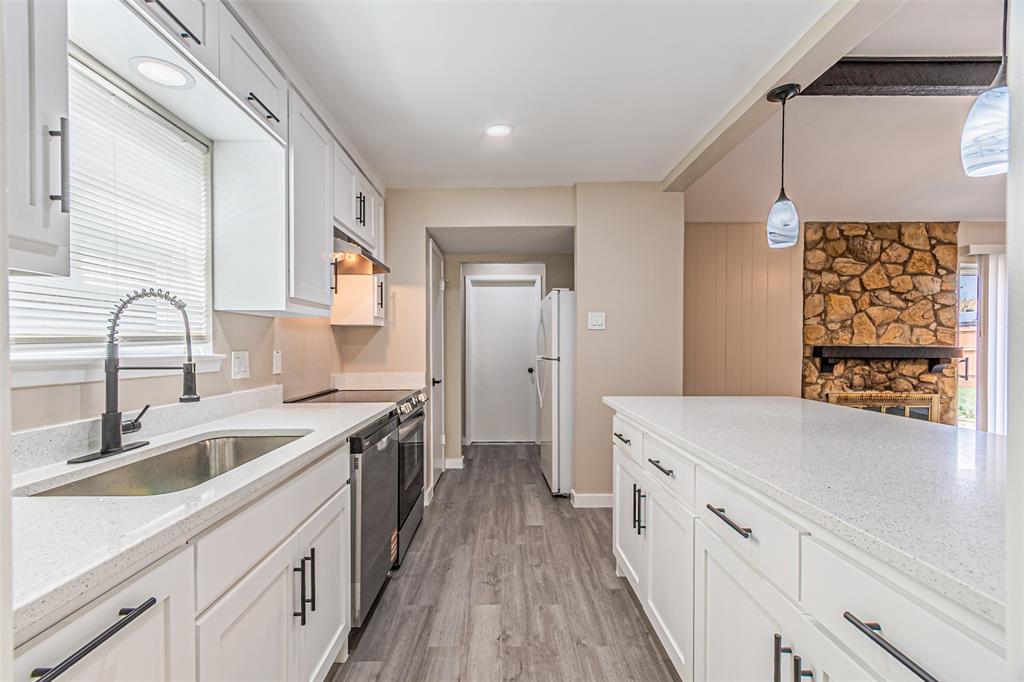 Kitchen featuring white shaker-style cabinetry, solid-surface countertops, wood-finish flooring, a high-arc pull-down faucet, and a stone-accented fireplace