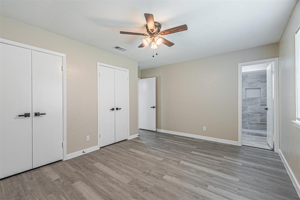 Room featuring wood-finish flooring, a ceiling fan with integrated lighting, dual closet doors with matte black hardware, and an entry to a tiled shower area