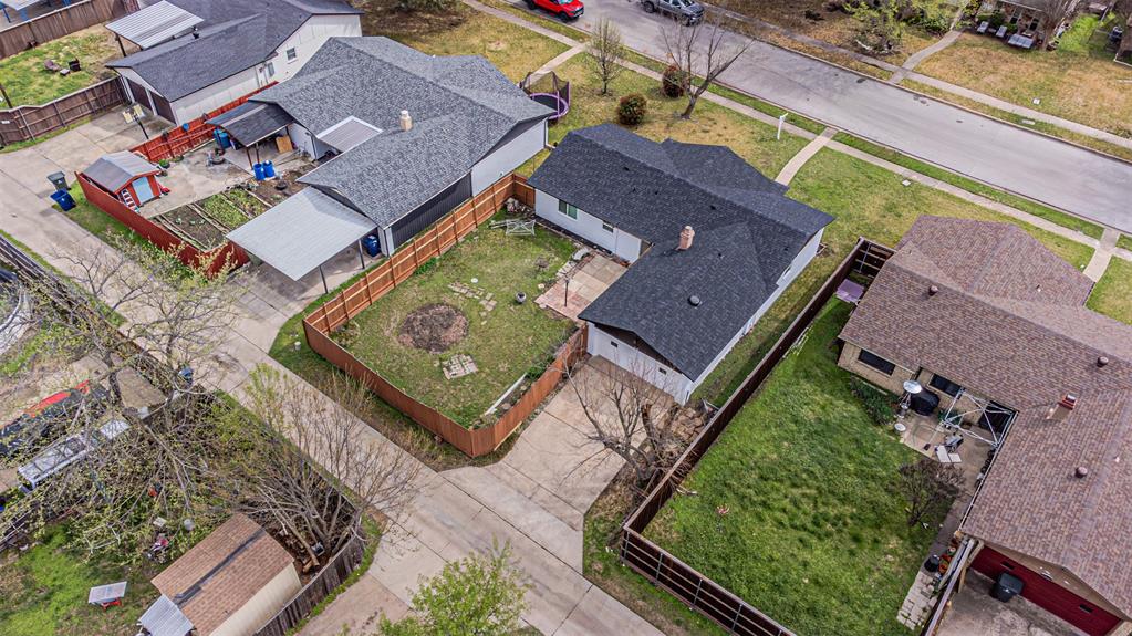 Aerial view of a residential lot featuring a concrete driveway, a fenced backyard, and a shingled roof