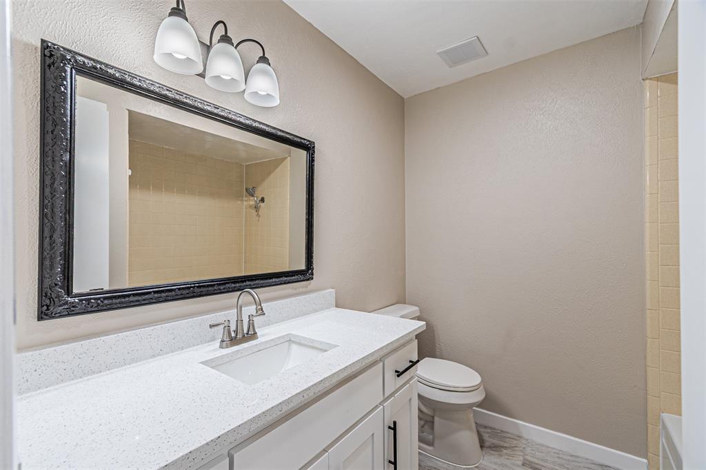 Bathroom featuring a vanity with a white countertop and rectangular undermount sink, black-framed mirror, three-light fixture, and tile shower surround