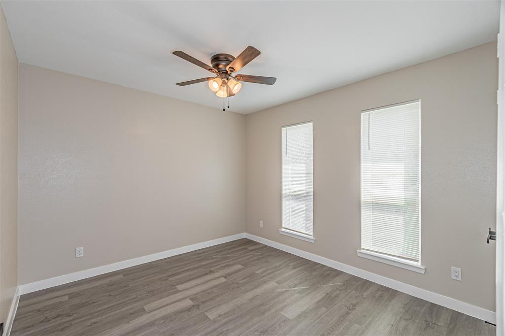 Neutral-toned interior space featuring wood-finish flooring, dual windows with integrated blinds, and a multi-light ceiling fan