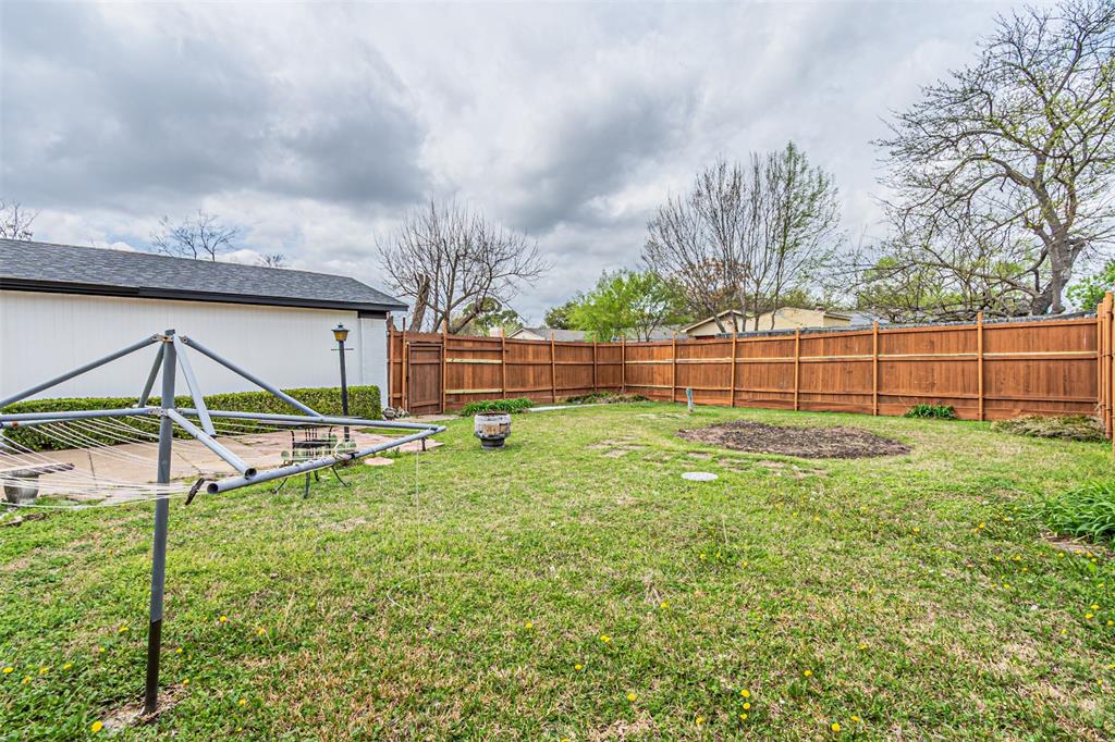 Backyard area featuring a wood-panel privacy fence, paved patio, and mature trees