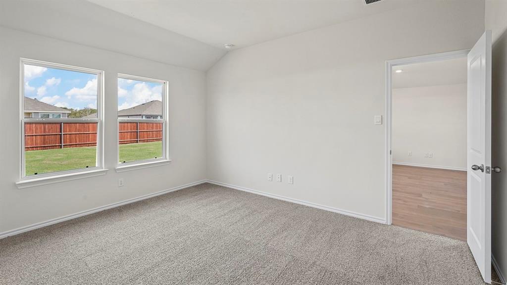 Vaulted ceiling featuring neutral wall-to-wall carpeting, dual windows, and a doorway revealing wood-finish flooring