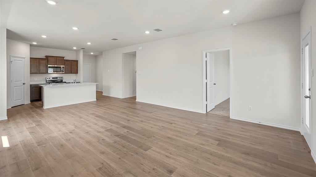 Open-concept area featuring wood-finish flooring, recessed lighting, a kitchen island with stone-finish countertops, and shaker-style cabinetry