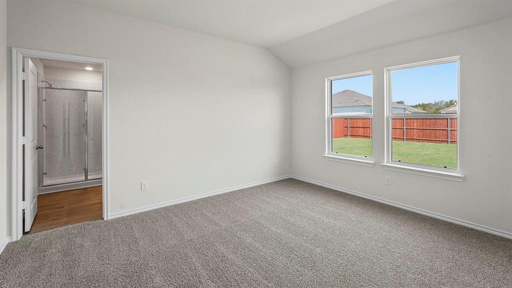 Neutral-toned carpeting, vaulted ceiling, dual-pane windows, and a doorway opening to a bathroom with a glass-enclosed shower